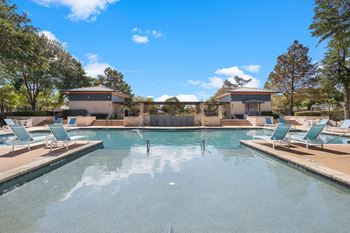 a large swimming pool with chairs and trees in the background at Artisan Apartments & Shops, Austin, TX 78729